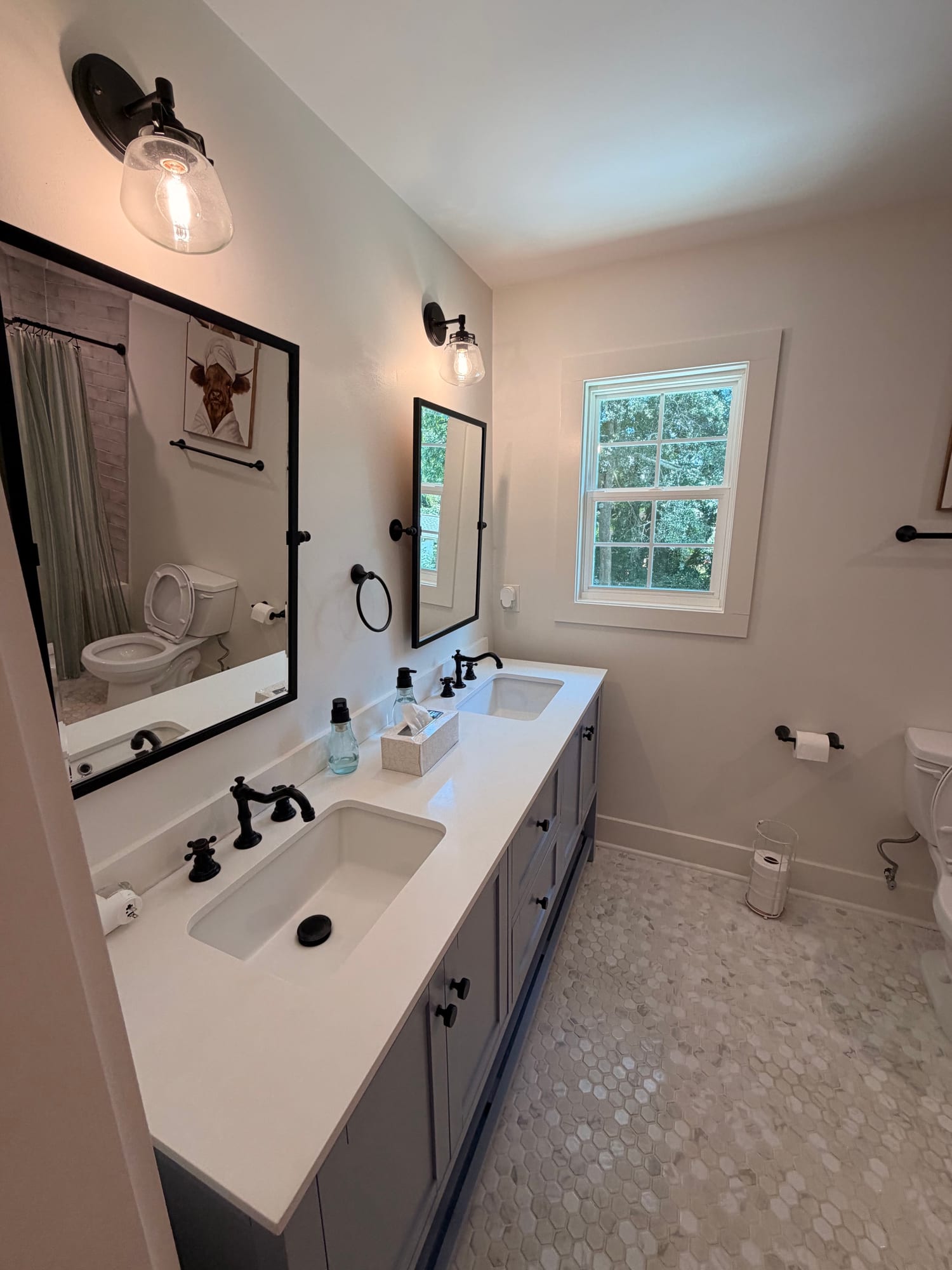 Rebuilt bathroom with a double vanity in stone, black-framed mirrors, wall sconces between them and a pebble-set floor.