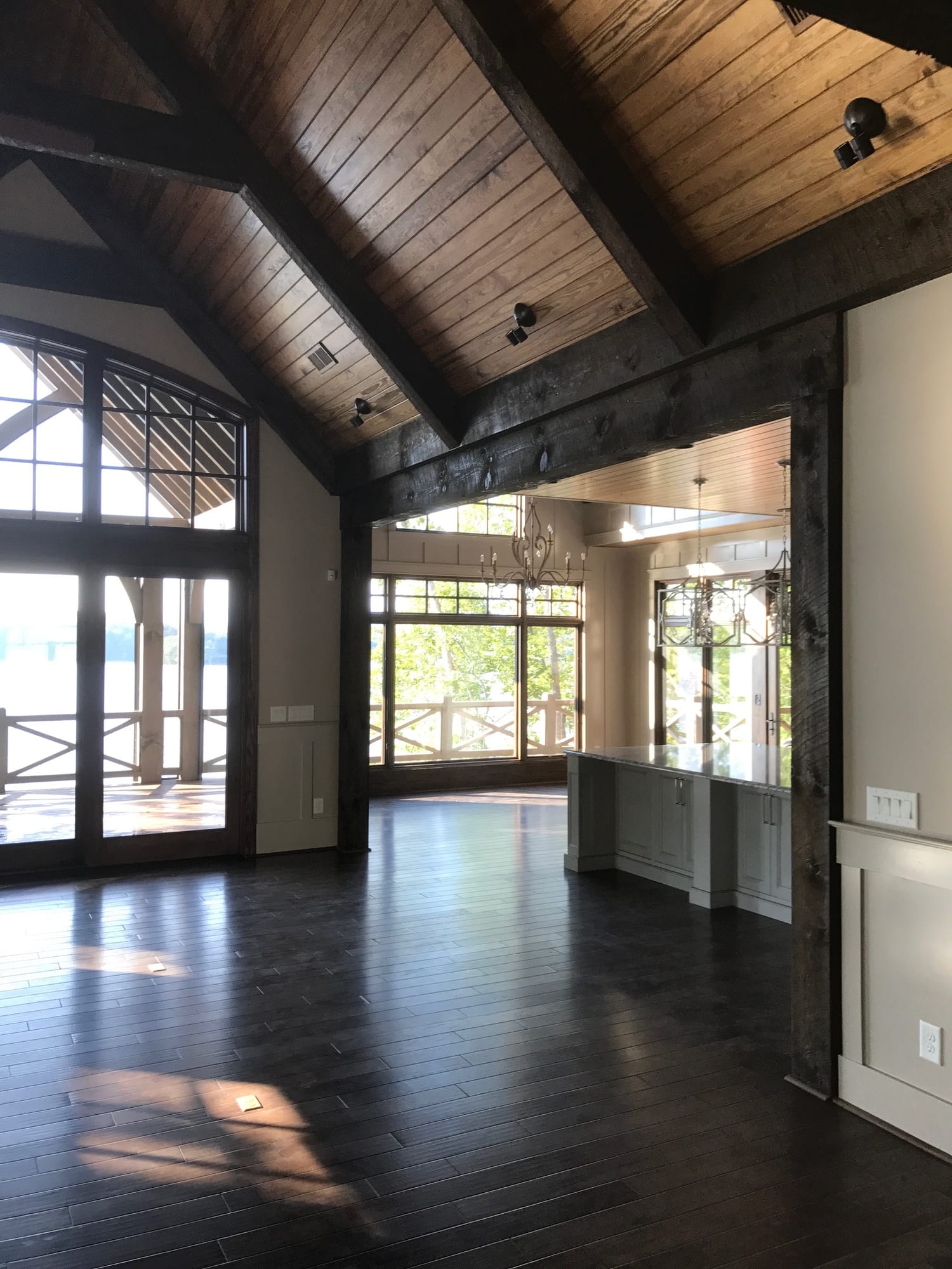 Great room with a vaulted tongue-and-groove ceiling and exposed timber trusses, opening through glazed doors to a covered porch and the lake.