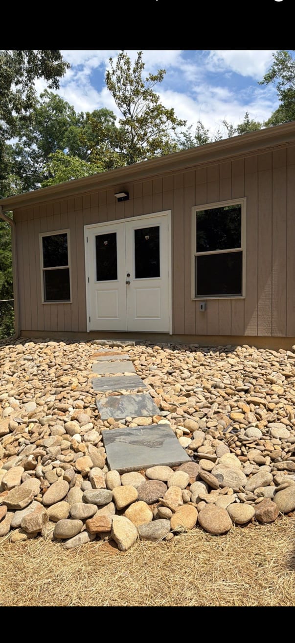 Finished detached workshop clad in board-and-batten with glazed doors, approached over a stone stepping path set through river rock.