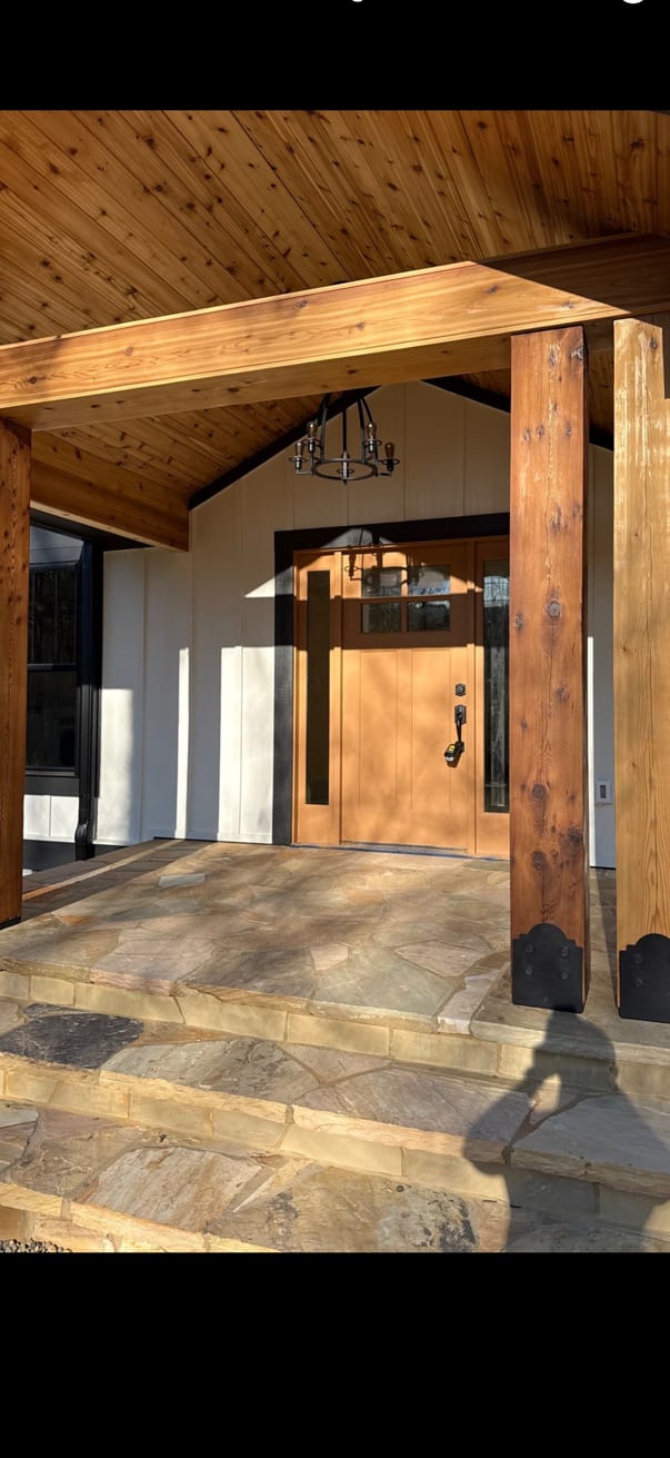 Entry hall framed by heavy timber posts under a stained tongue-and-groove ceiling, with a lantern hung over a stone floor.