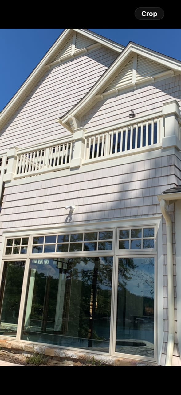 Rear elevation of a lakeside house in white lap siding, with stacked gables, a railed balcony and glazing carried up through both storeys.