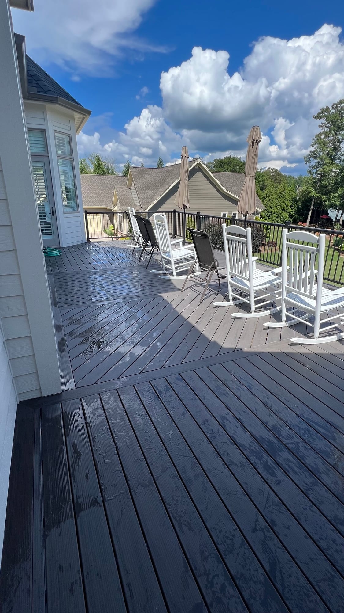 Dark-stained deck boards running to a black rail, with white rocking chairs and umbrellas set along the edge under a clear sky.