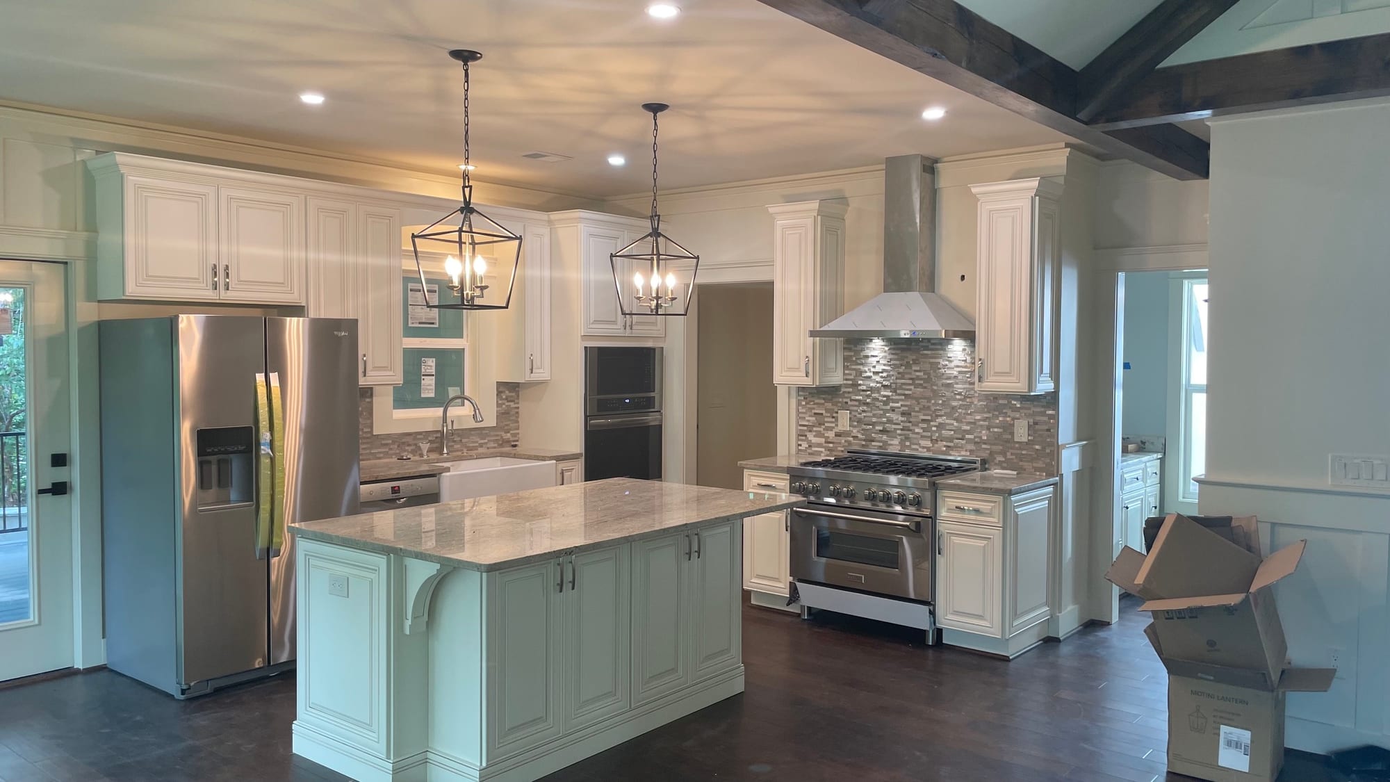 Finished kitchen with a painted island, stone counters, lantern pendants and a stainless range under a hood.