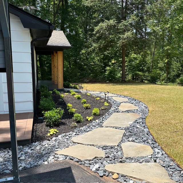 Finished house in white board-and-batten with dark trim, a flagstone path set through river rock and fresh planting to either side.
